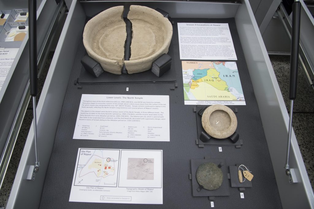 Photograph of an open exhibit drawer with four ancient objects from Nippur accompanied by exhibit labels.