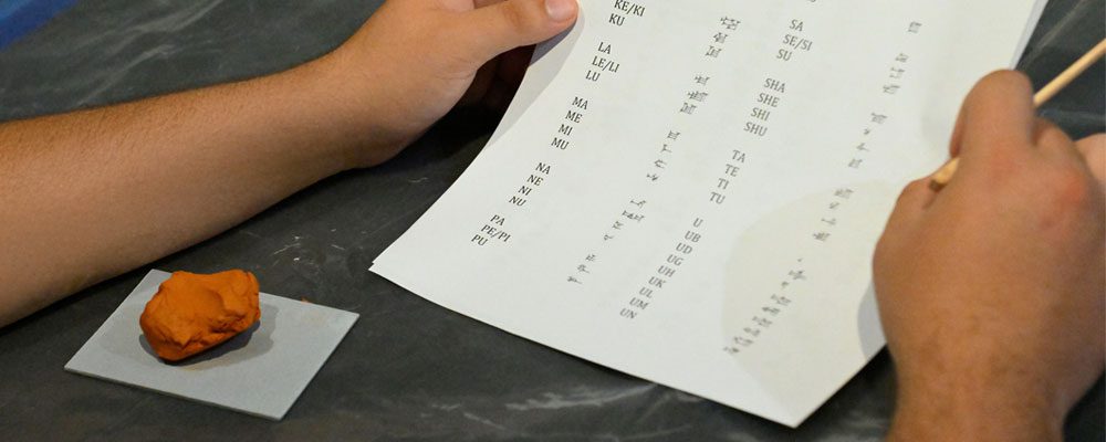 Hands of student holding a paper with letterforms and a ball of clay in front of them.