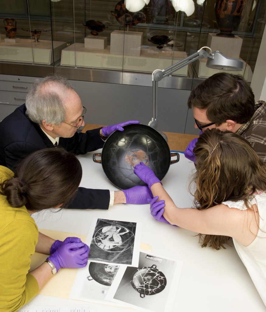 Photograph of a man in a museum holding an Ancient Greek kylix while two women and one man look on.