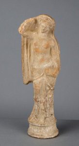 Ancient Greek terracotta statue of a standing draped figure with one hand raised, wearing a flowing garment.