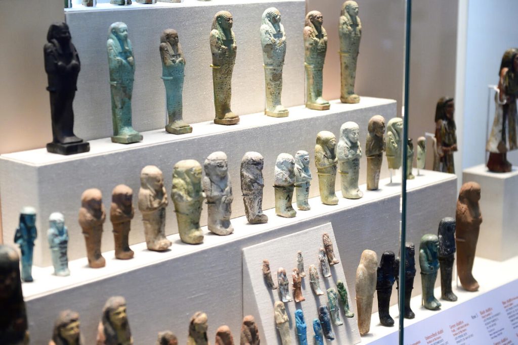 View of an exhibit case showing 3 rows of ancient Egyptian shabti funerary figurines.