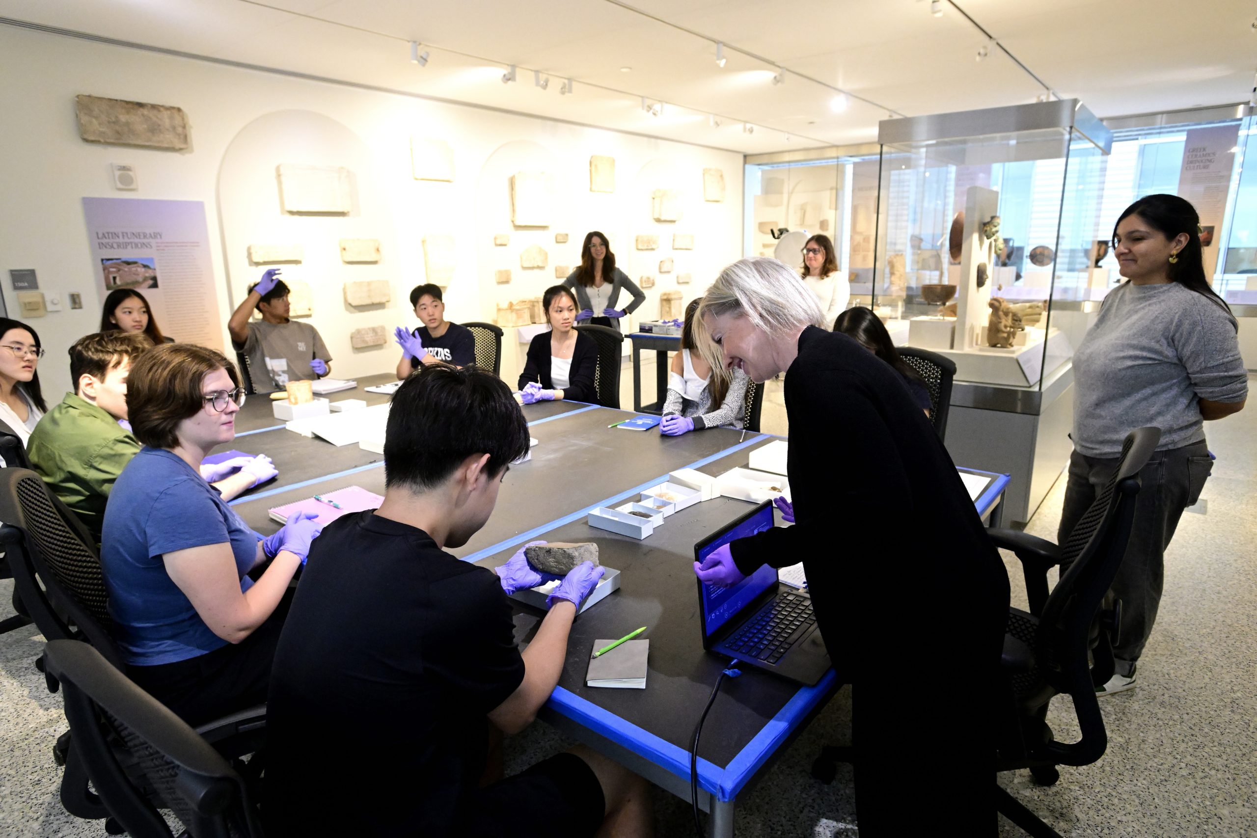 Overview of a class seated at a table inside the museum working with ancient objects.