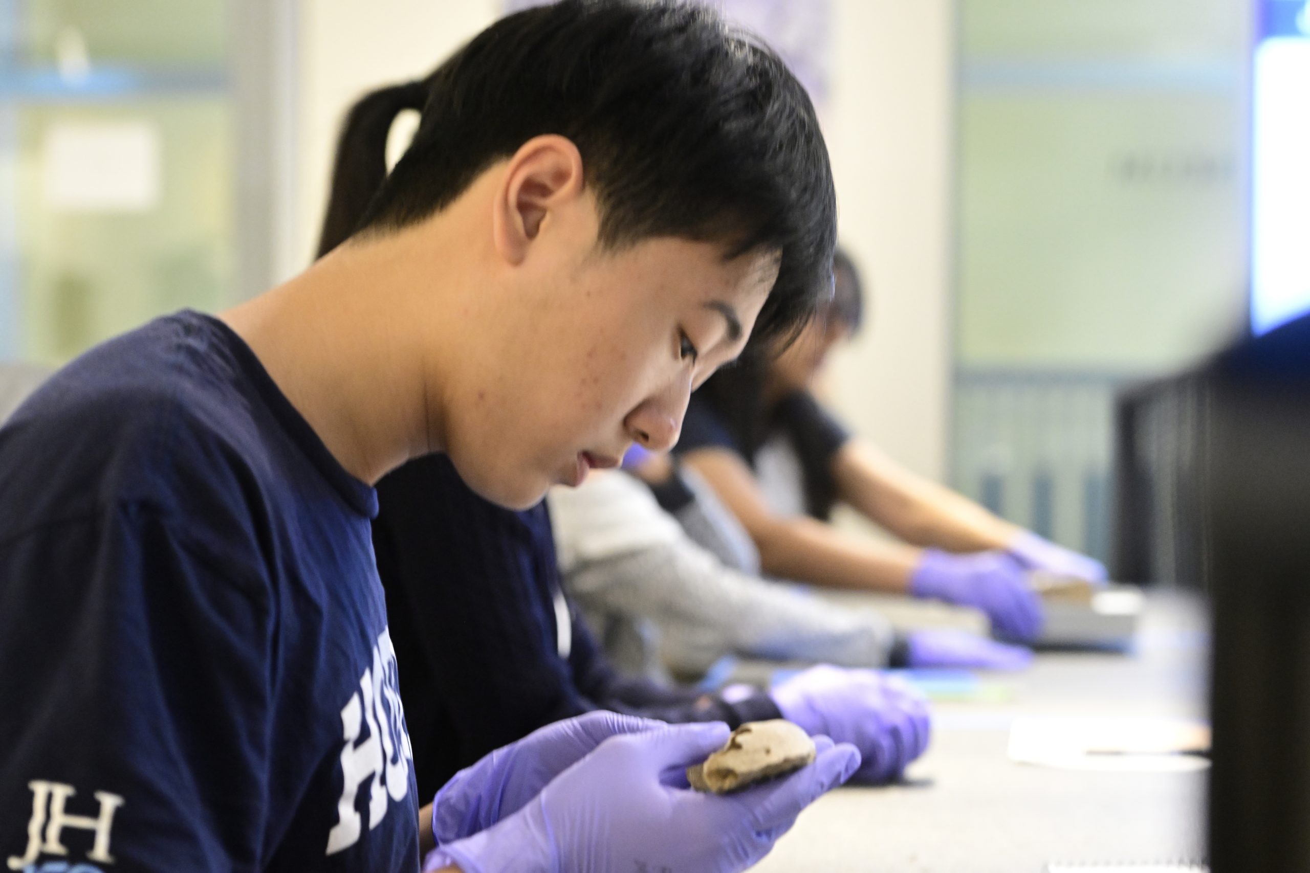 Closeup of a male student sitting at a table wearing purple nitrile gloves holding an ancient artifact.