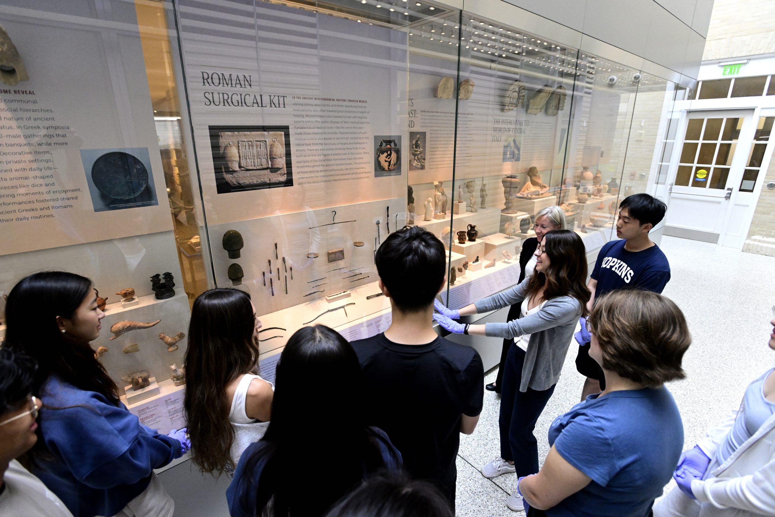 Photo of a class and instructors standing in the hallway looking at a museum exhibit case.