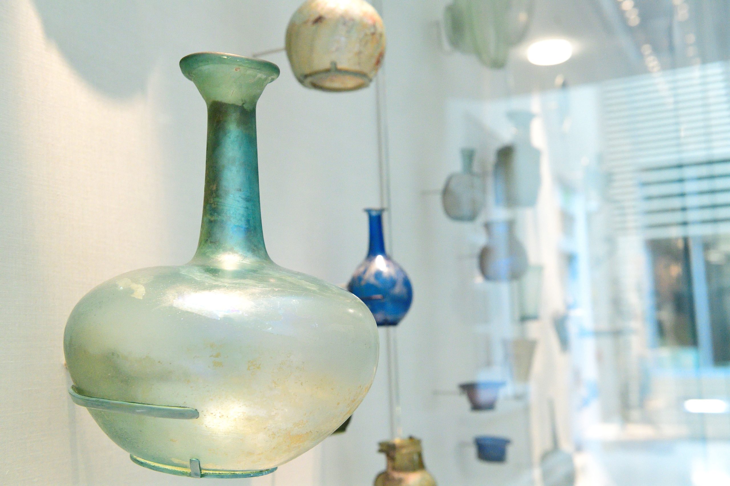 Angled view of a museum display case featuring ancient Roman glass objects of various colors.